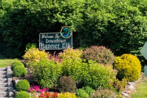 A sign saying "Welcome to Downtown Banner Elk" surrounded by beautiful shrubbery, trees, and flowers